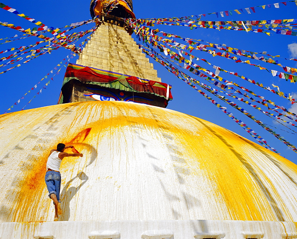 Young man throwing saffron water on the stupa in order to purify it before ritual, Bodhnath, Katmandu, Nepal