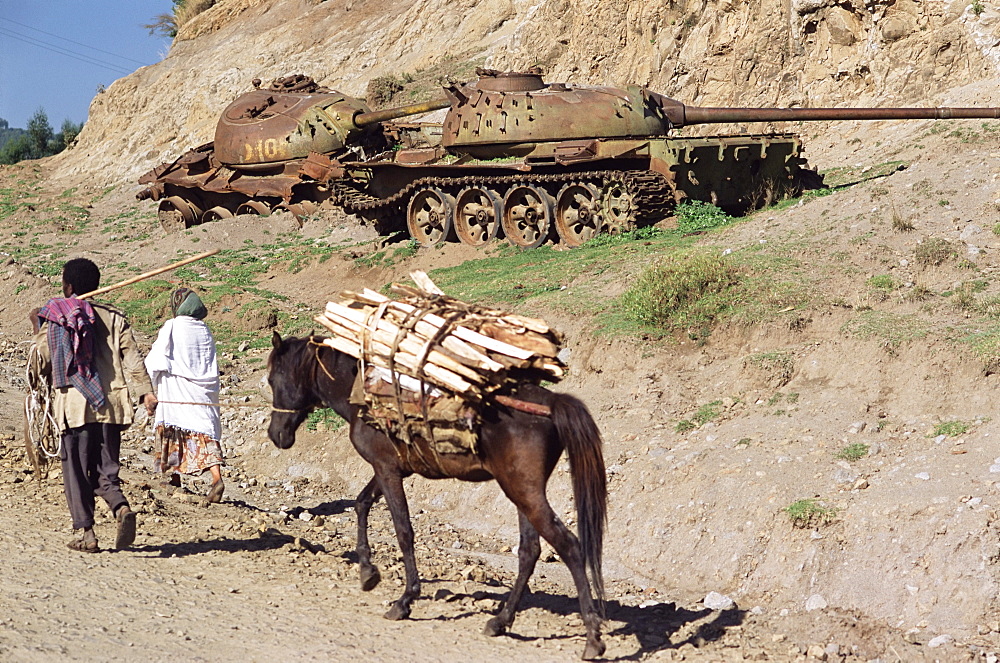 Horse carrying wood passes rusting tank from the war, Sentebe, Choa region, Ethiopia, Africa