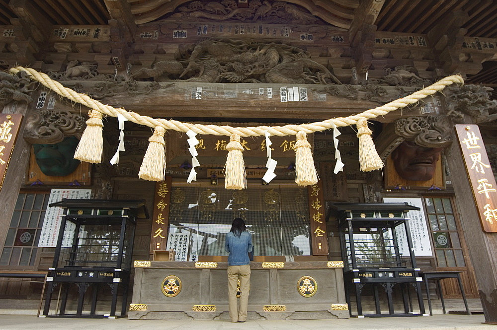 Girl praying at shrine under giant rope, Takao jinja shrine, Takao San mountain, Tokyo, Japan, Asia