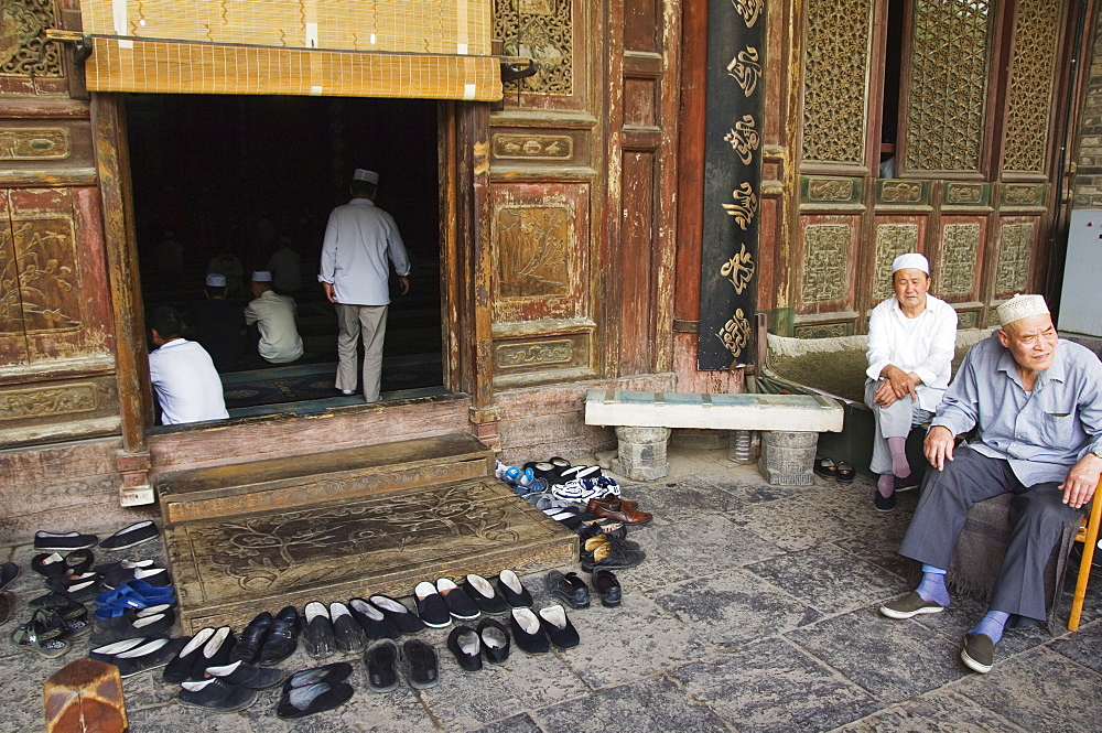 Men praying and shoes left outside at The Great Mosque located in the Muslim Quarter home to the city's Hui community, Xian City, Shaanxi Province, China, Asia