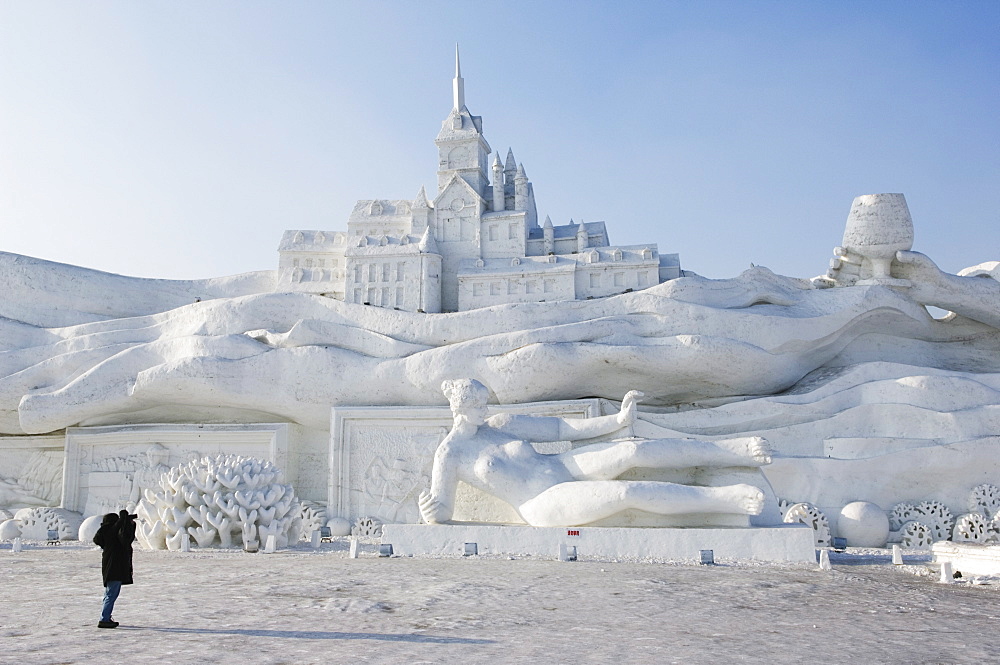 A lone person photographing a giant sculpture at Snow and Ice Sculpture Festival on Sun Island Park, Harbin, Heilongjiang Province, Northeast China, China, Asia