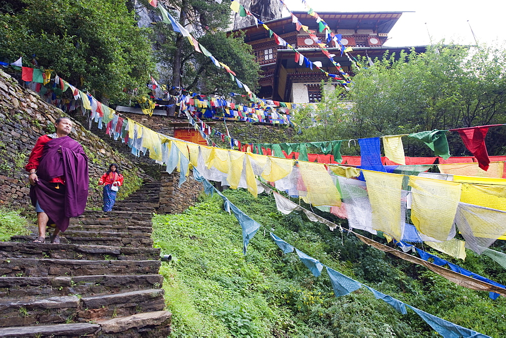 A monk walking through prayer flags, Tigers Nest, Taktsang Goemba, Paro Valley, Bhutan, Asia