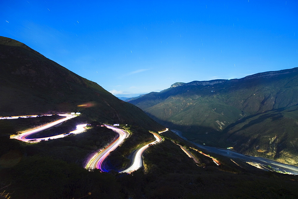 Moonlit valley and car light trails on a winding road in Chicamocha National Park, Colombia, South America