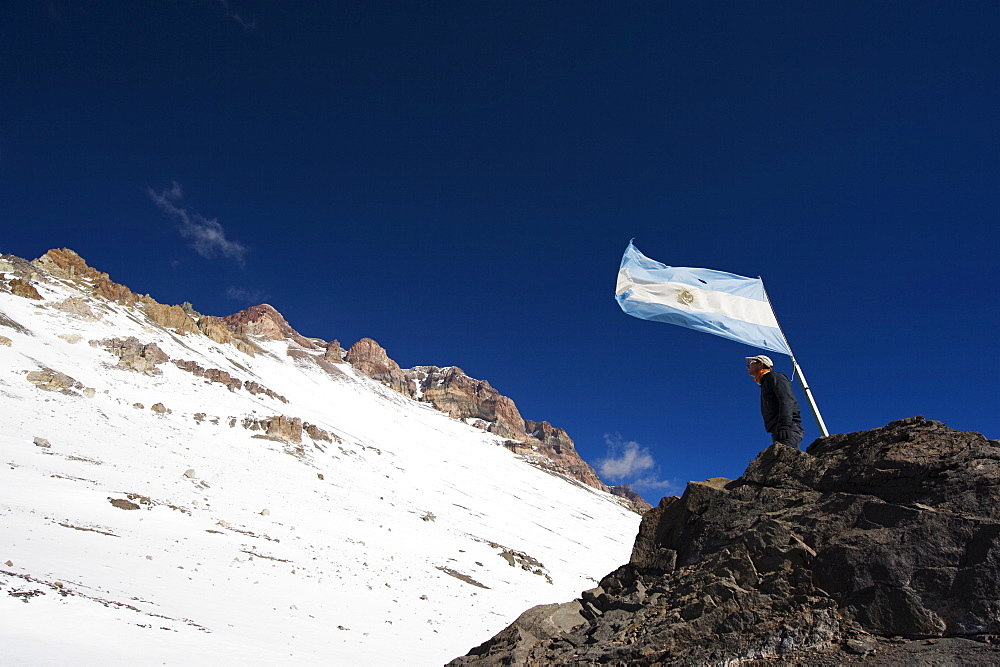 Hiker under the Argentinian flag looking up at the summit of Aconcagua 6962m, highest peak in South America, Aconcagua Provincial Park, Andes mountains, Argentina, South America