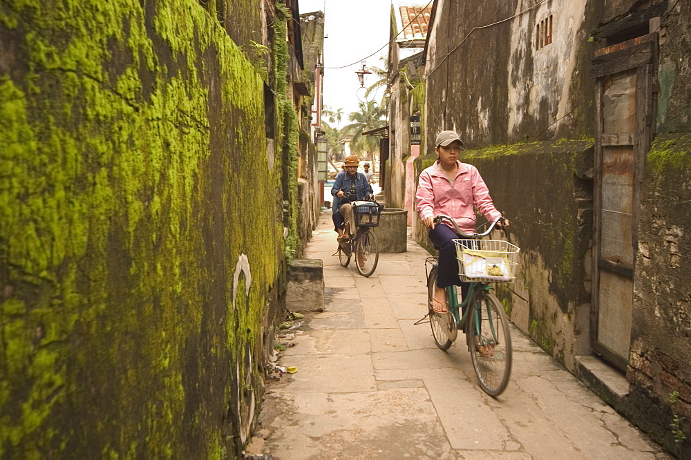 Cycling through moss covered alley, Hoi An, Vietnam, Southeast Asia, Asia