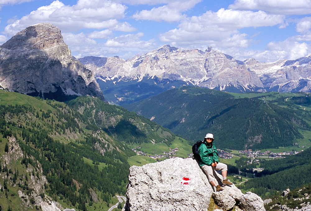 Hiker resting at Alta Via Dolomiti (Via Ferrata) trail with Corvara village below, Dolomites, Alto Adige, Italy, Europe