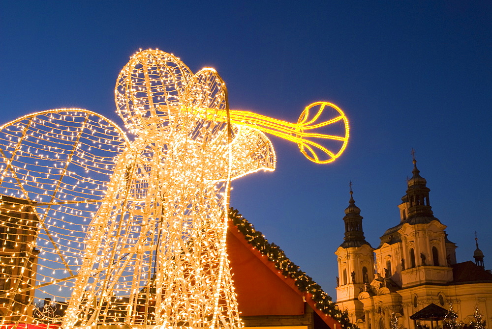 Glowing angel, part of Christmas decoration at Staromestske (Old Town Square) with Baroque St. Nicholas church at twilight, Stare Mesto, UNESCO World Heritage Site, Prague, Czech Republic, Europe