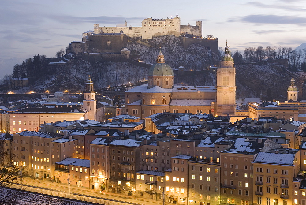 Snow covered Old Town with towers of Glockenspiel, Dom and Franziskanerkirche churches dominated by the fortress of Festung Hohensalzburg at twilight, Salzburg, Austria, Europe