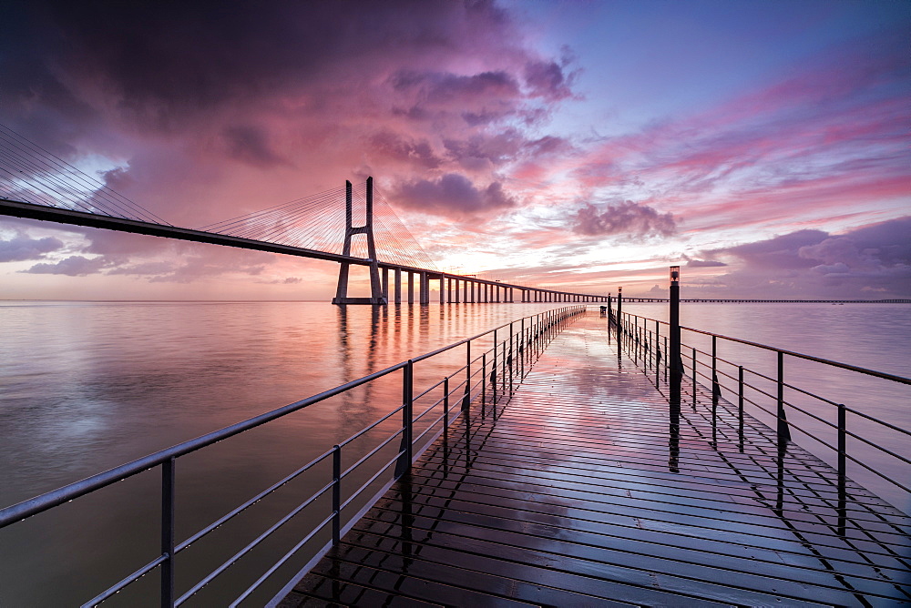 Sunrise colors the clouds reflected in Tagus River and frame the Vasco da Gama bridge in Lisbon, Estremadura, Portugal, Europe