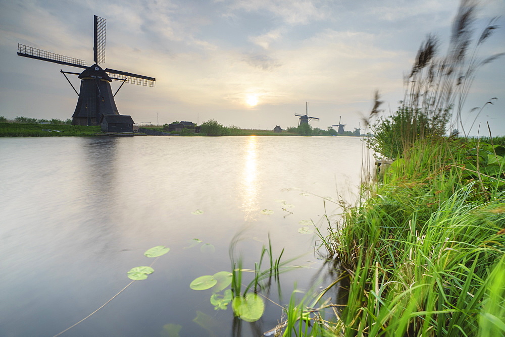 Morning sun just risen shines in the canal where windmills are reflected Kinderdijk, Rotterdam, South Holland, Netherlands, Europe