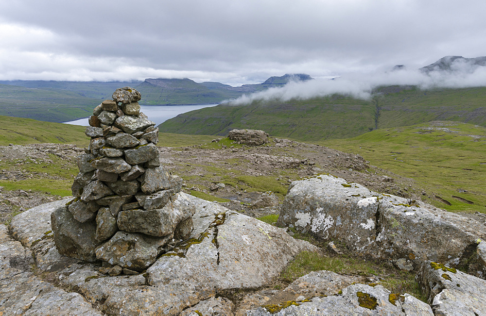 View over the Vestmannsund towards the island Streymoy, Cairn in the mountains of Vagar, part of the Faroe Islands. Cairns are the traditional markers of the old trails network connecting the villages of Faroe.  Europe, Northern Europe, Denmark, Faroe Islands