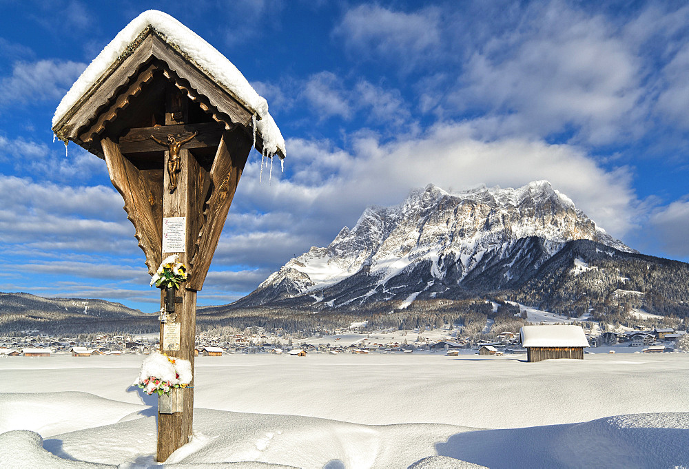 Wetterstein mountain chain with Mt. Zugspitze from Ehrwald with wayside cross, Austria. Zugspitze, the highest mountain in Germany, is in the background in the left. The cablecar from Ehrwald to Zugspitze is visible on the left. The village Ehrwald is a famous tourist destination in summer and winter, Austria, Tyrol, Ehrwald