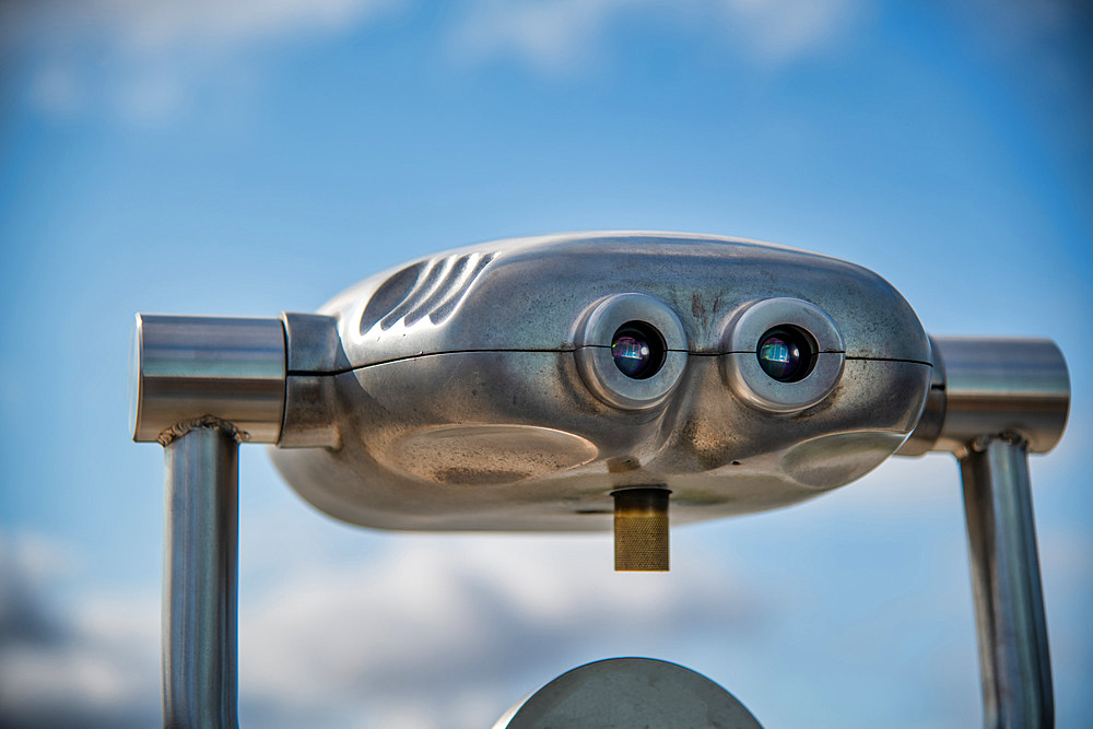 Shiny binocular telescope against blue sky.