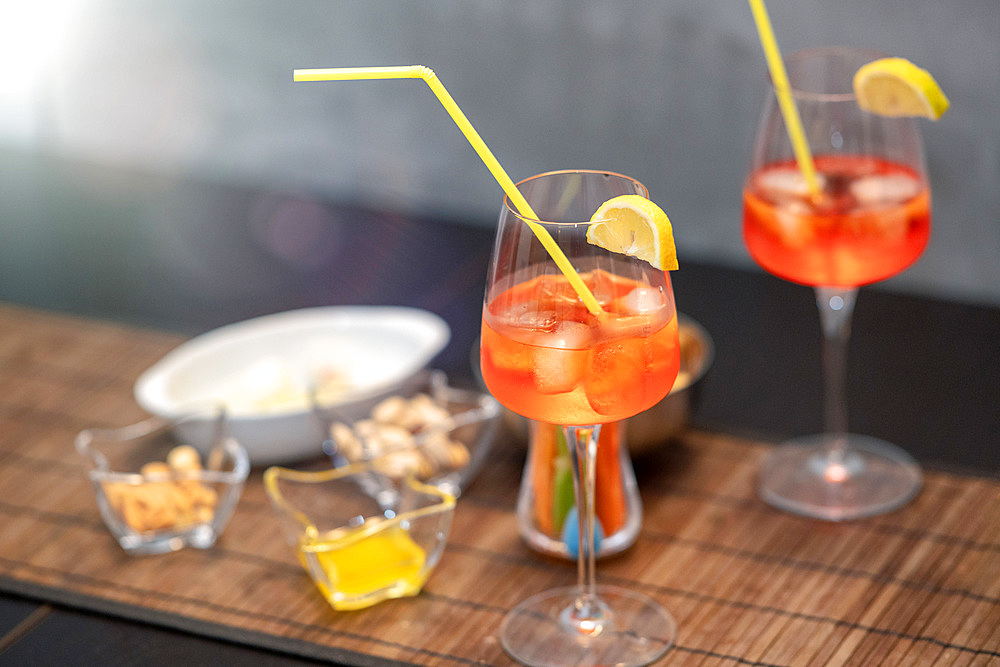 Closeup of some glasses with cocktails with straws and nuts on a brown table.