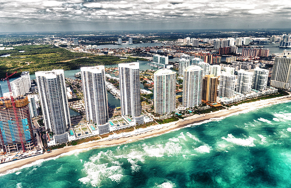 Aerial view of North Miami Beach skyscrapers with sun and clouds.