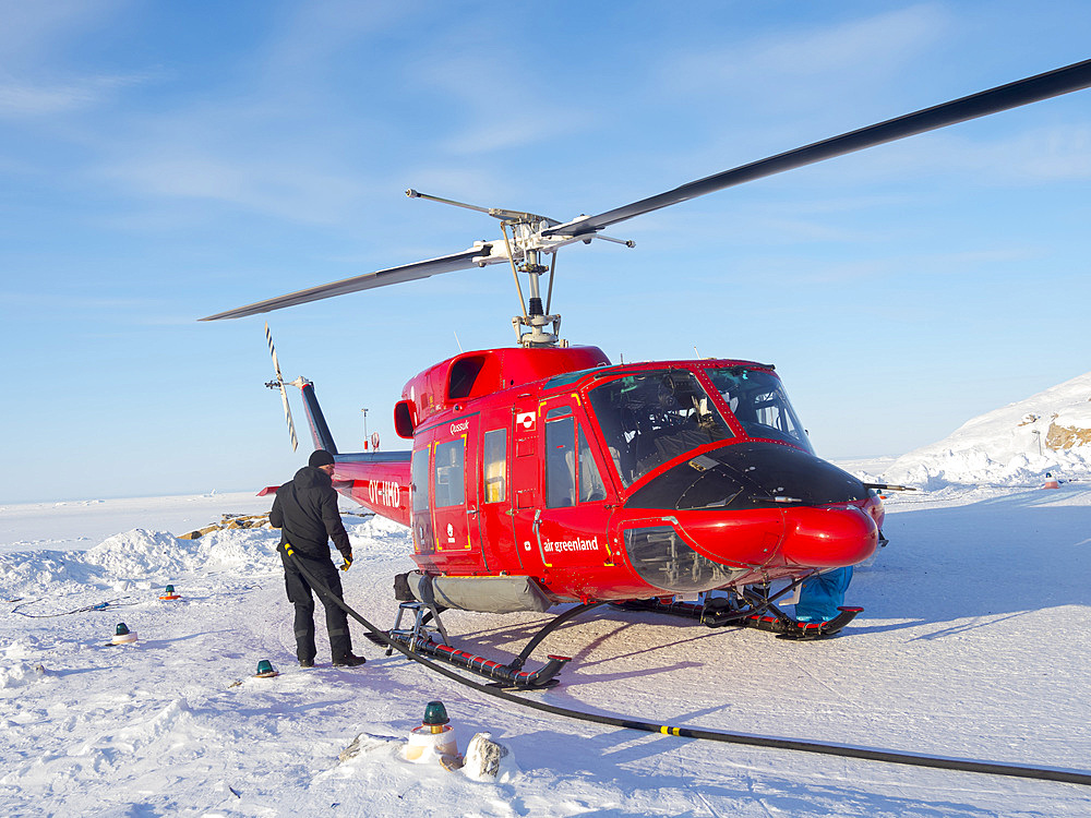 Pilots are refueling the helicopter on the helipad. During winter the helicopter is the only link to the rest of Greenland. The traditional village Kullorsuaq on the shore of the Melville Bay, part of the Baffin Bay, in the far north of Greenland.