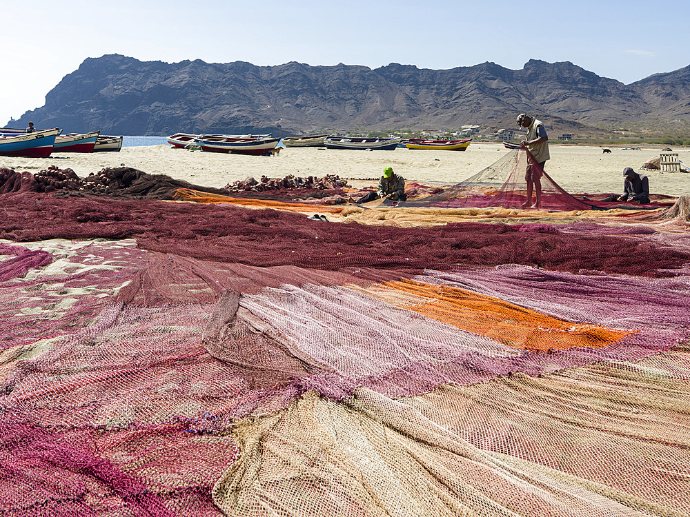 Fishermen are mending their colorful fishing nets on a beach near Sao Pedro. Island Sao Vicente, Cape Verde an archipelago in the equatorial, central Atlantic in Africa.