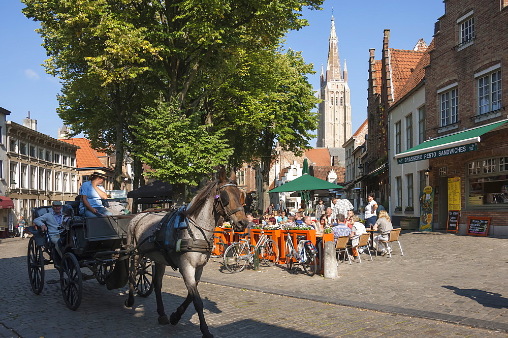 Square with cafe, horse and carriage, and spire of Church of Our Lady, Bruges, Belgium, Europe