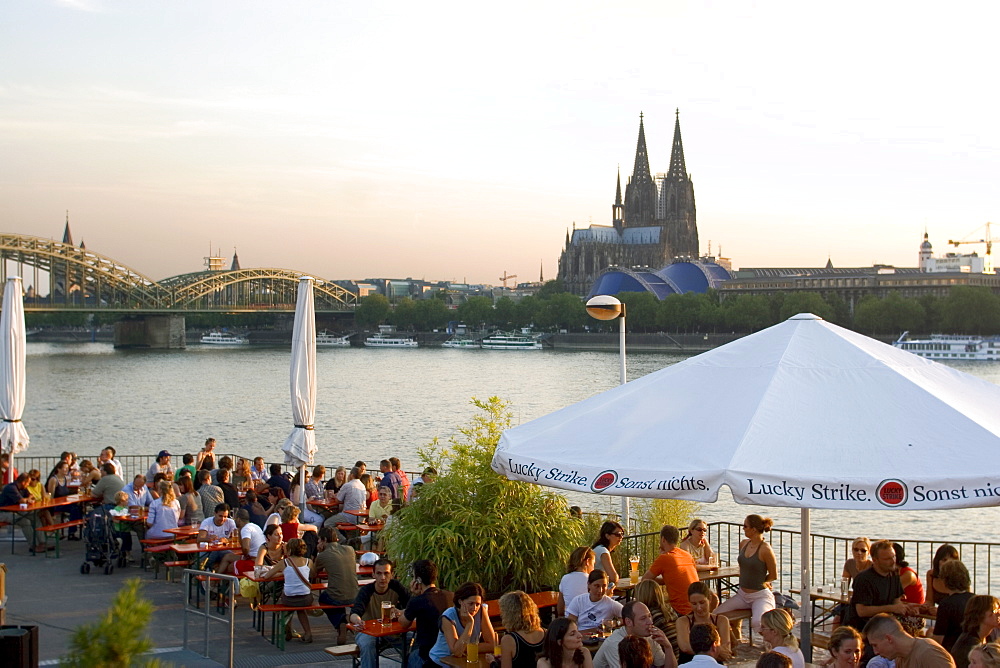 People at trendy Rheinterrassen bar and restaurant beside the River Rhine, with the old town and cathedral beyond, Cologne, North Rhine Westphalia, Germany