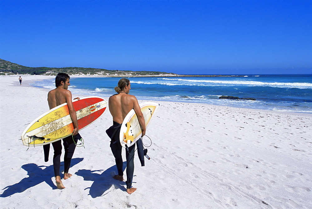 Two surfers walking with their boards on Kommetjie beach, Cape Town, South Africa, Africa