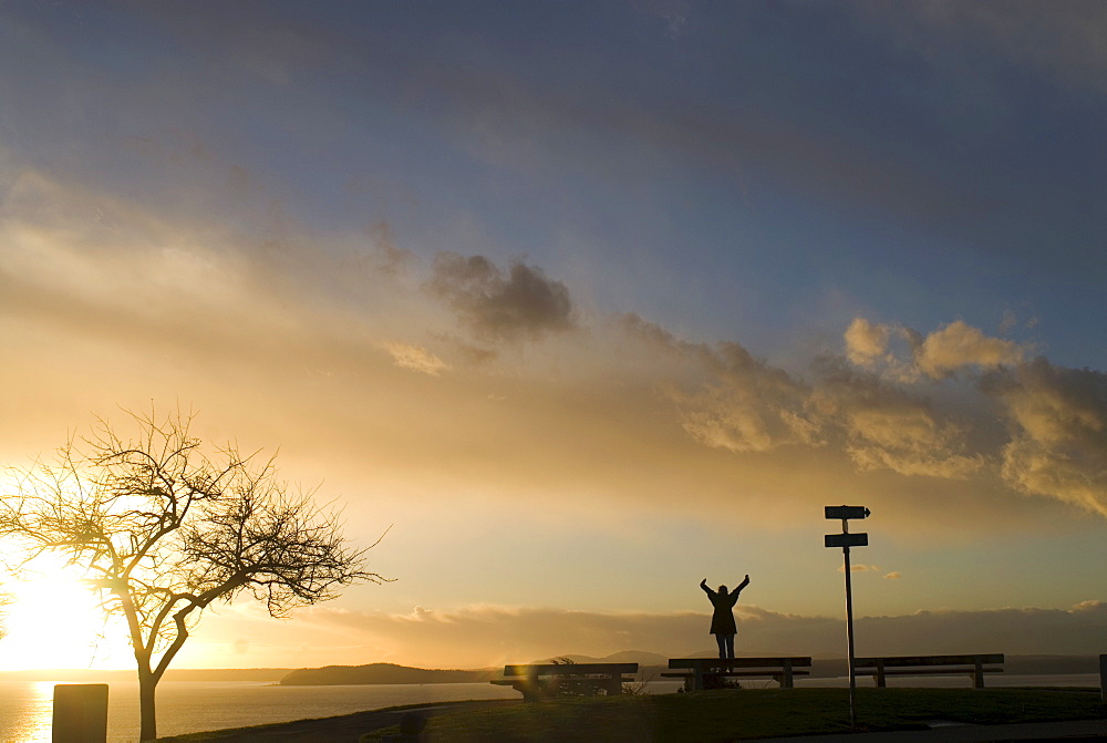 Silhouette of girl stretching at sunset, Puget Sound, with Blake Island in distance, Upper Queen Anne, Seattle, Washington. United States of America, North America