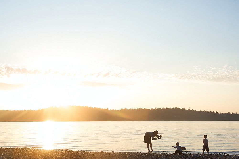 Silhouette of mother taking pictures of children at sunset, Vashon Island, Washington State, United States of America, North America