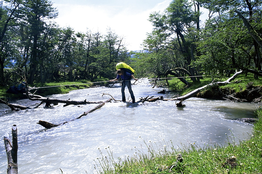 Backpacker crosses log bridge on circuit around the park, Torres del Paine National Park, Chile, South America