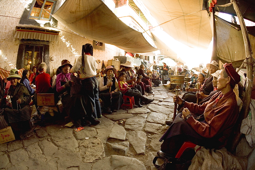 Pilgrims spin prayer wheels outside a monastery in the Bharkor, Lhasa, Tibet, China, Asia