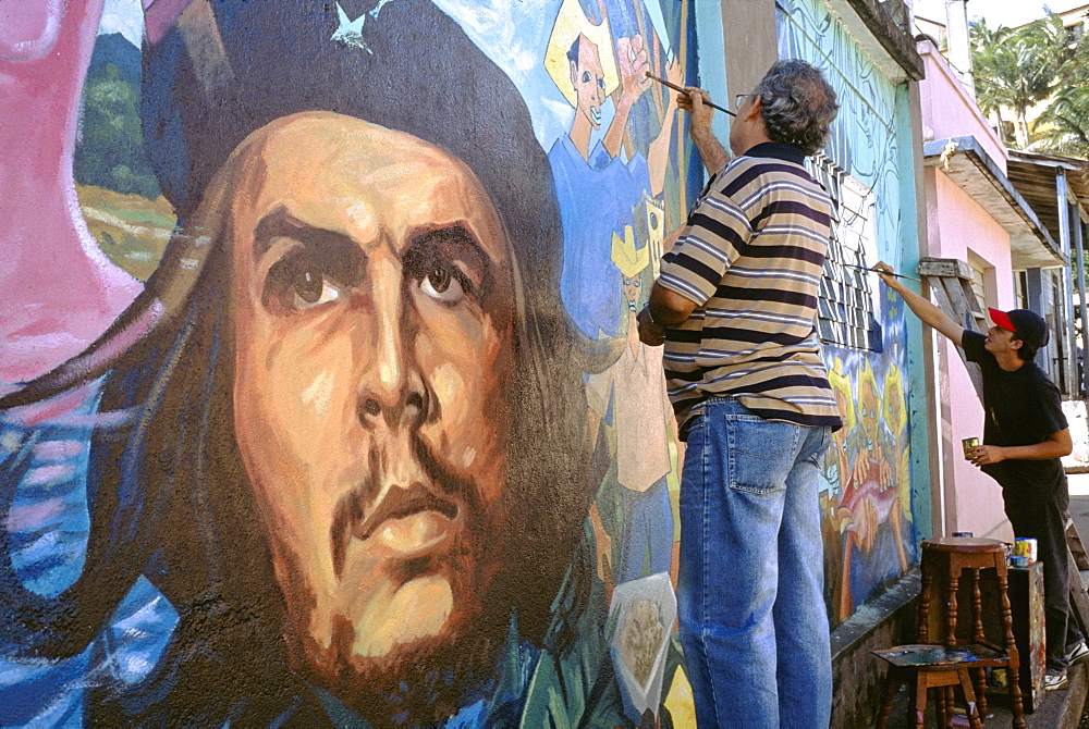 An artist painting a wall mural featuring a portrait of the revolutionary hero Che Guevara on a street in Baracoa, Cuba