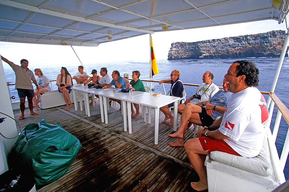 Dive master explaining to scuba divers the characteristics of their next dive site off volcanic rock called Roca Redonda, Galapagos Islands, Ecuador