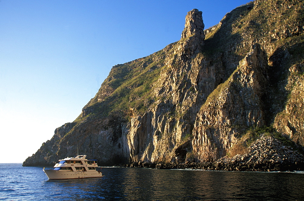 Steep, rugged, volcanic cliffs surround Wolf Island one of the newest and most northerly of the Galapagos with scuba diving boat, Galapagos Islands, Ecuador