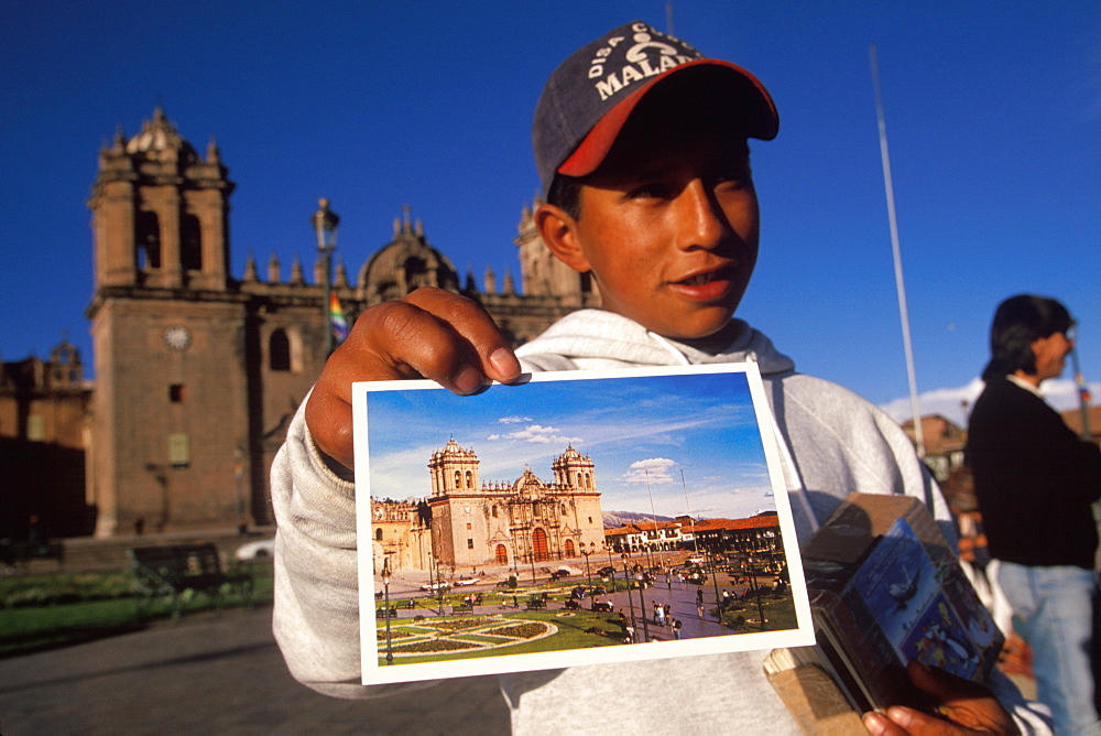 Ancient capital of the Incas the Plaza de Armas with a young boy selling postcards of the Cathedral with the Cathedral beyond, Cuzco, Highlands, Peru