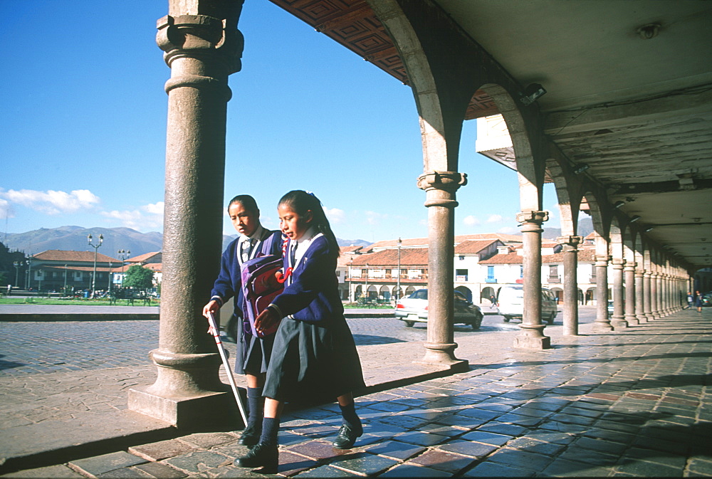 The Plaza de Armas, in the old colonial city with two young school girls walking under arcade, Cuzco, Highlands, Peru