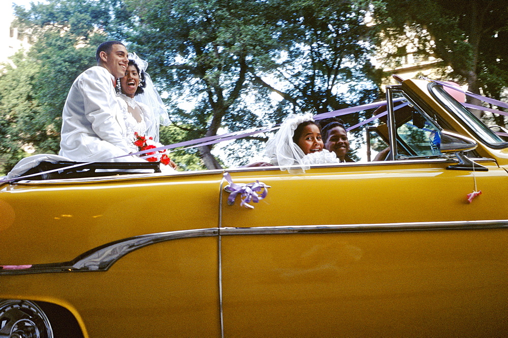 Just married bride and groom after wedding ceremony riding in back seat of vintage American car in Centro Habana, Havana, Cuba