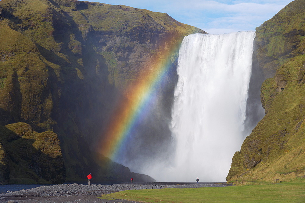 Tourist in red jacket at 62 m high Skogafoss waterfall, Skogar, South area, Iceland, Polar Regions