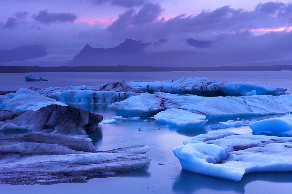 Icebergs in Jokulsarlon glacial lagoon, at dusk, Oraefajokull (Vatnajokull) glacier in the distance, East Iceland, Iceland, Polar Regions