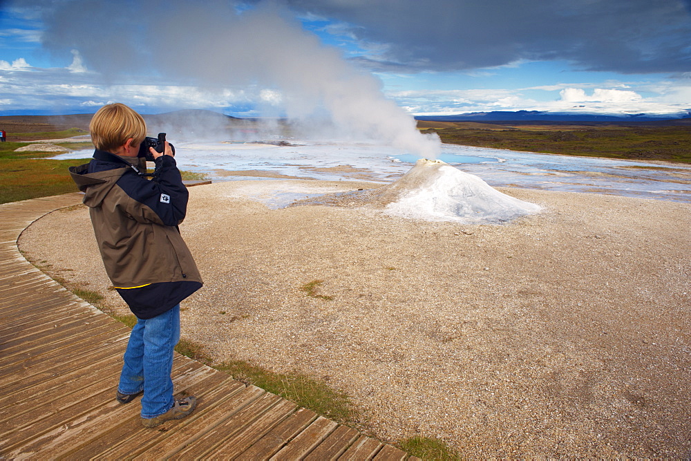 A young boy taking pictures of Oskurholshver (screaming spring), famous hot spring at Hveravellir, Kjolur, Iceland, Polar Regions