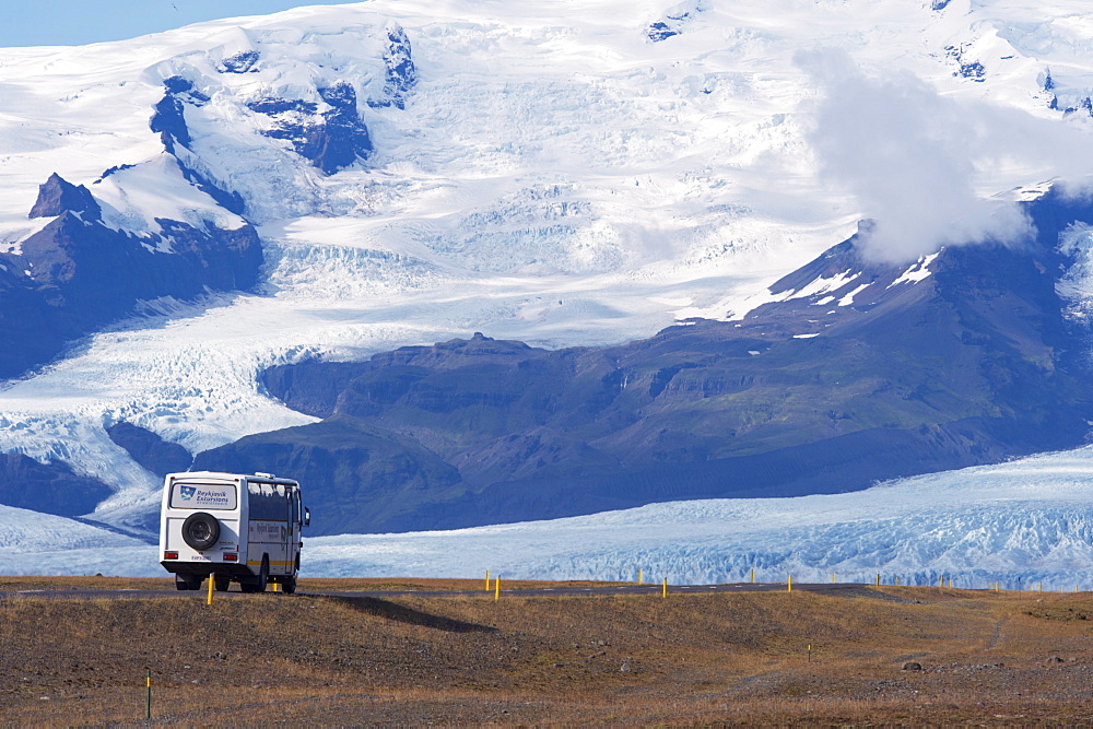 A tourist bus on the ring road (Route 1) beneath the huge mass of Oraefajokull (Vatnajokull) glacier, south-west Iceland (Austurland), Iceland, Polar Regions