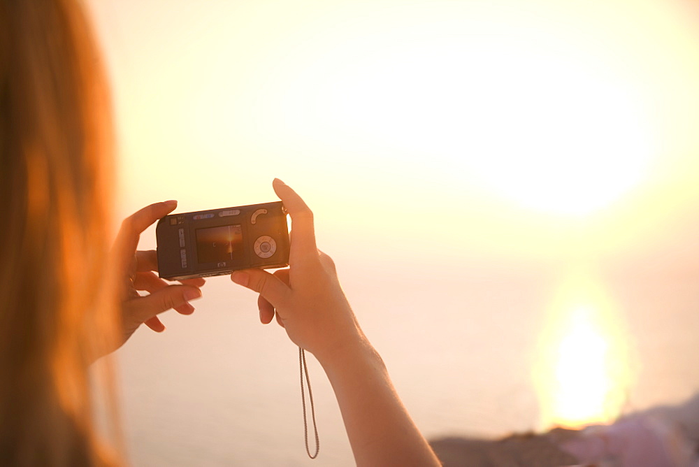 Woman taking photograph of sunset, Oia, Santorini (Thira), Cyclades Islands, Greek Islands, Greece, Europe