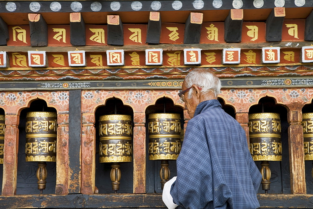 Old Bhutanese man turning prayer wheels in Buddhist temple, Thimphu, Bhutan, Asia