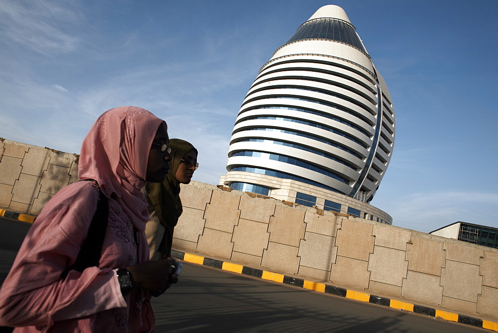 Locals walk past the 5-star Boji Al-Fateh Hotel (Libyan Hotel), designed to represent a sail, Khartoum, Sudan, Africa