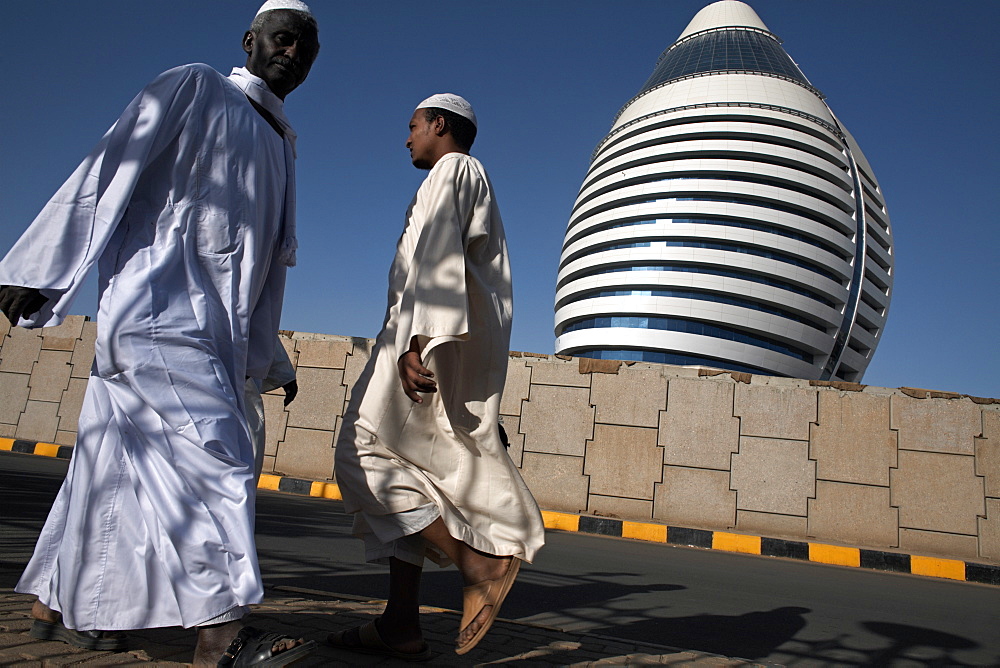 Locals walk past the 5-star Boji Al-Fateh Hotel (Libyan Hotel), designed to represent a sail, Khartoum, Sudan, Africa