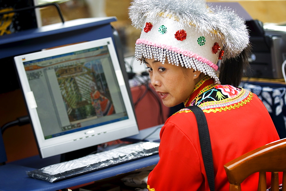 Woman in ethnic dress at computer, Kunming, Yunnan, China, Asia