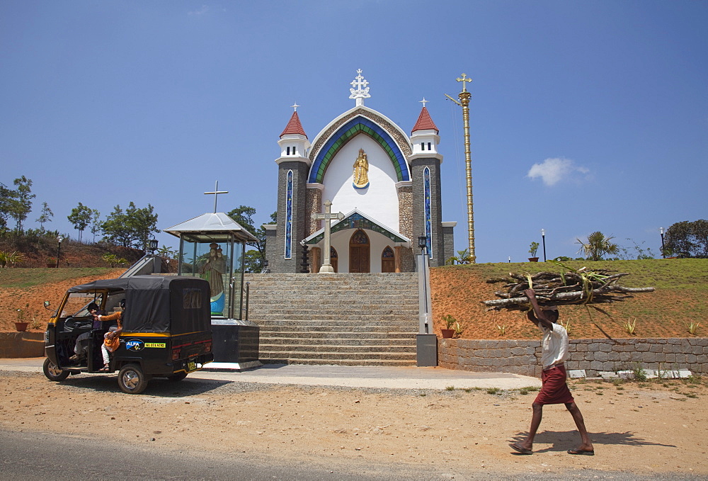 Man carrying firewood on his head walking past a church in rural Kerala, India, Asia 