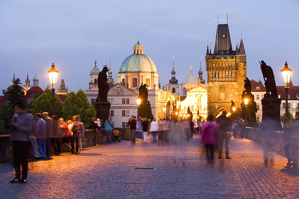 Statues and crowds on the Charles Bridge, with the dome of the Church of St. Francis and the Old Town Bridge Tower beyond, evening light, Old Town, Prague, Czech Republic, Europe