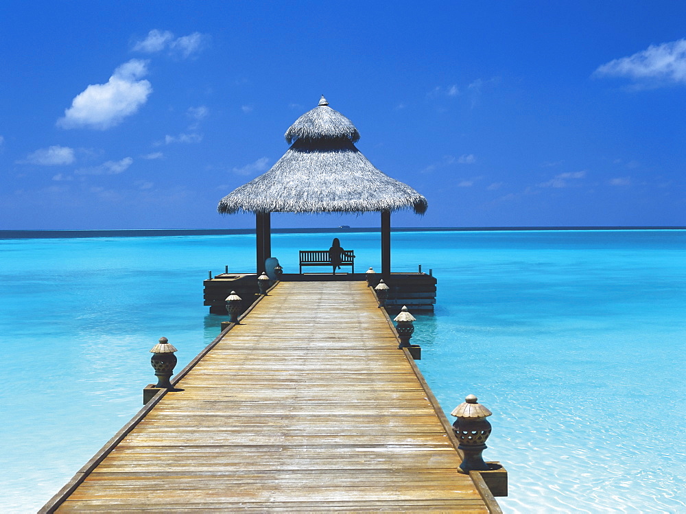 Young woman sitting on bench at the end of jetty, Maldives, Indian Ocean, Asia