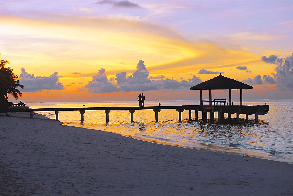 Couple on jetty looking at sunset, Maldives, Indian Ocean, Asia