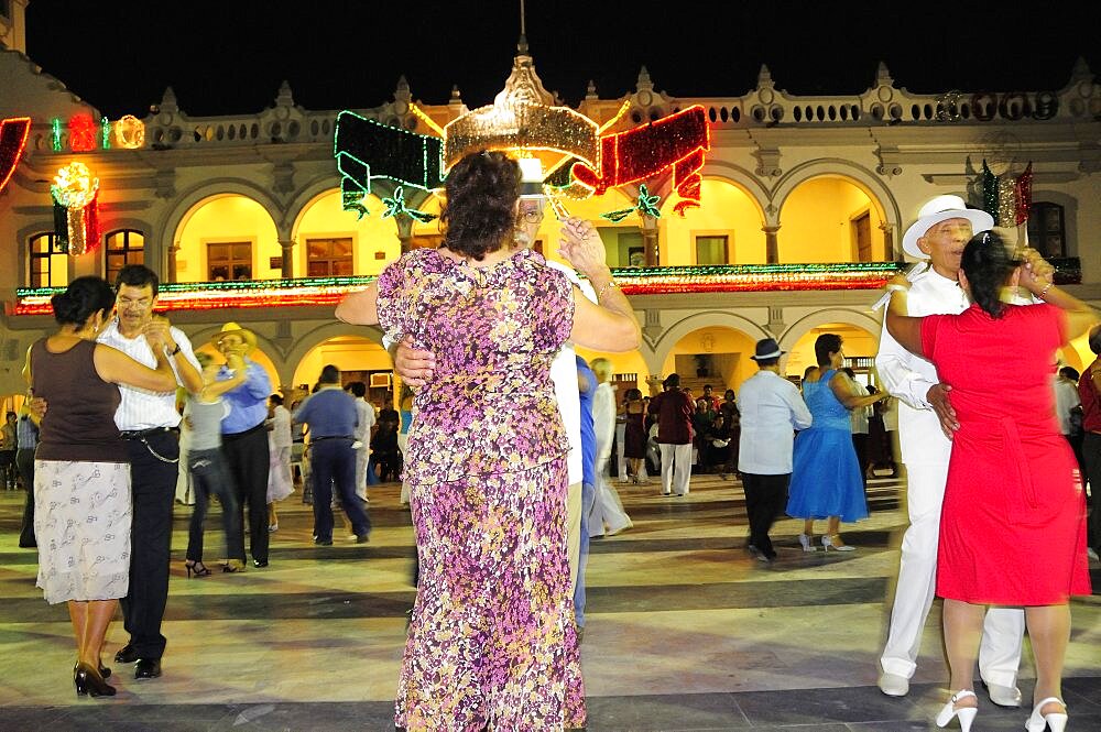 Mexico, Veracruz, Couples dancing in the Zocalo at night illuminated decorations in the national colours for Independence Day celebrations on building facade behind.