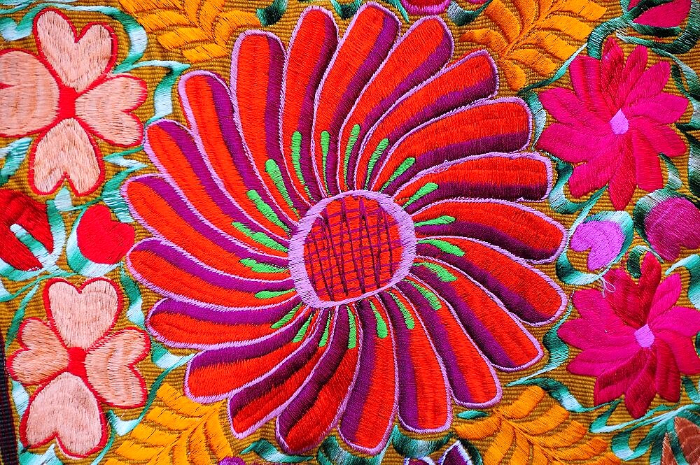 Mexico, Bajio, San Miguel de Allende, Detail of brightly embroidered textile in arts shop with flower design in pink red and orange.