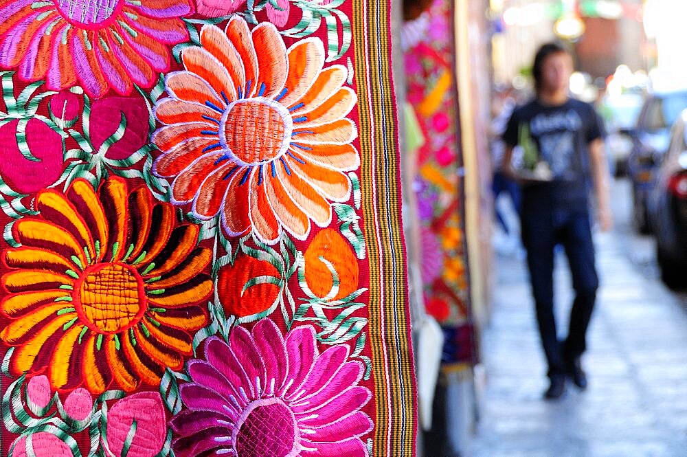 Mexico, Bajio, San Miguel de Allende, Brightly coloured embroidered textile hanging outside arts shop with flower design in pink red and orange.